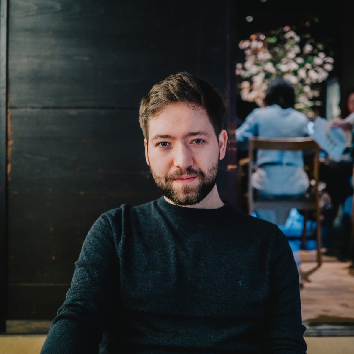 Benedict Couve in a dark sweater, seated at a wooden table in soft evening light