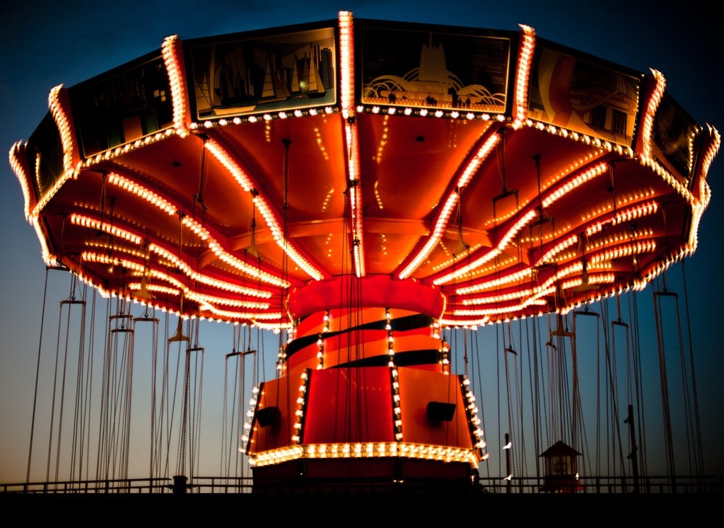A lit swing carousel turning against a deep blue sky