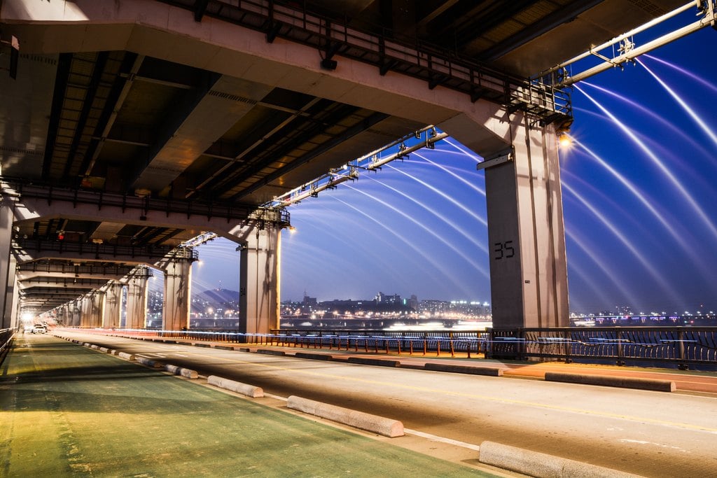 The underside of a bridge, its arches lit blue
