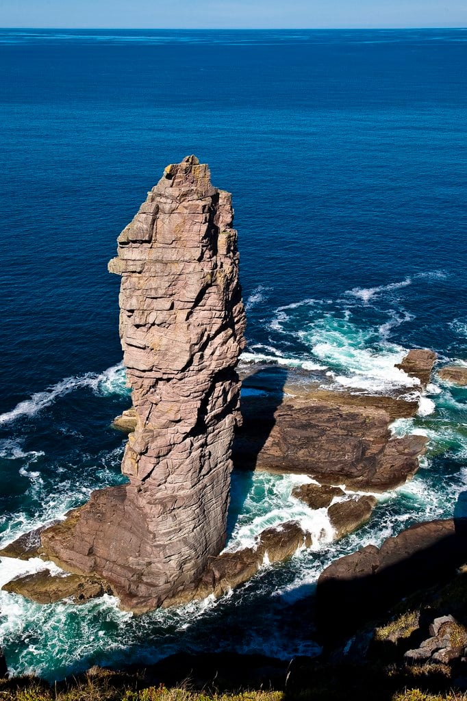 A lone sea stack rising from dark water below a cliff