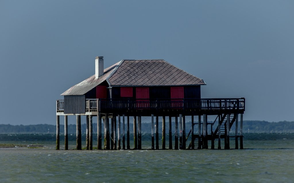 A red stilt house on thin legs above flat grey water
