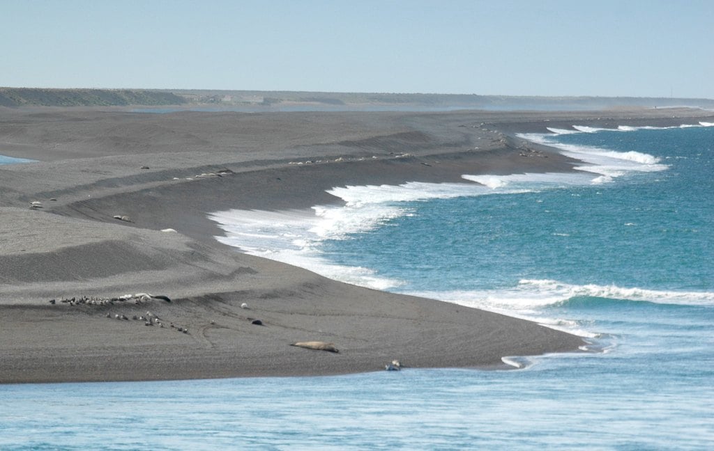 A wide grey beach curving away, surf rolling in
