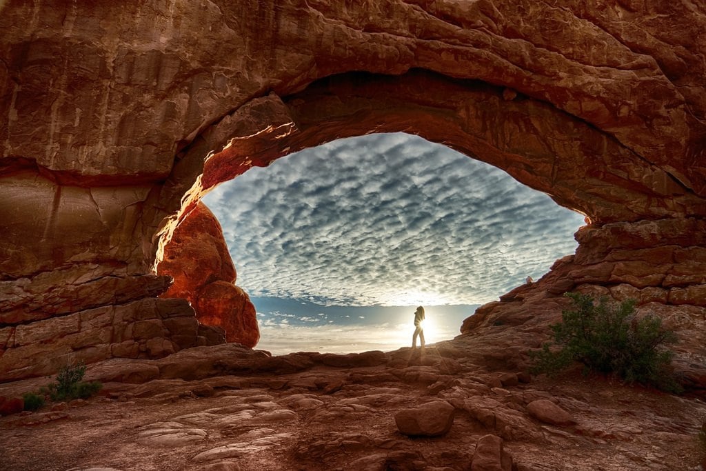 A sandstone arch framing a figure and a blue sky