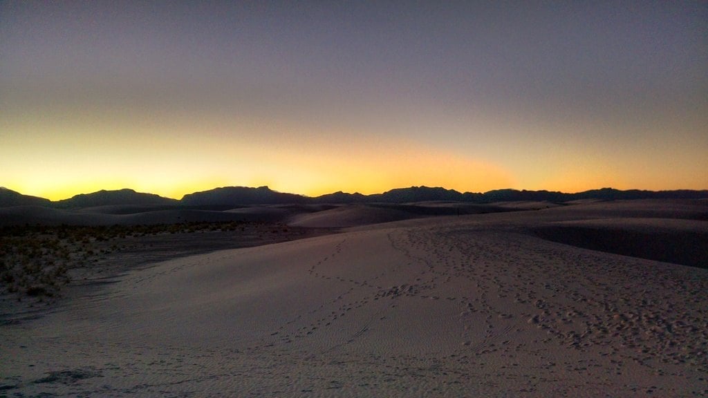 Dark dunes under a dusk sky with a band of orange light