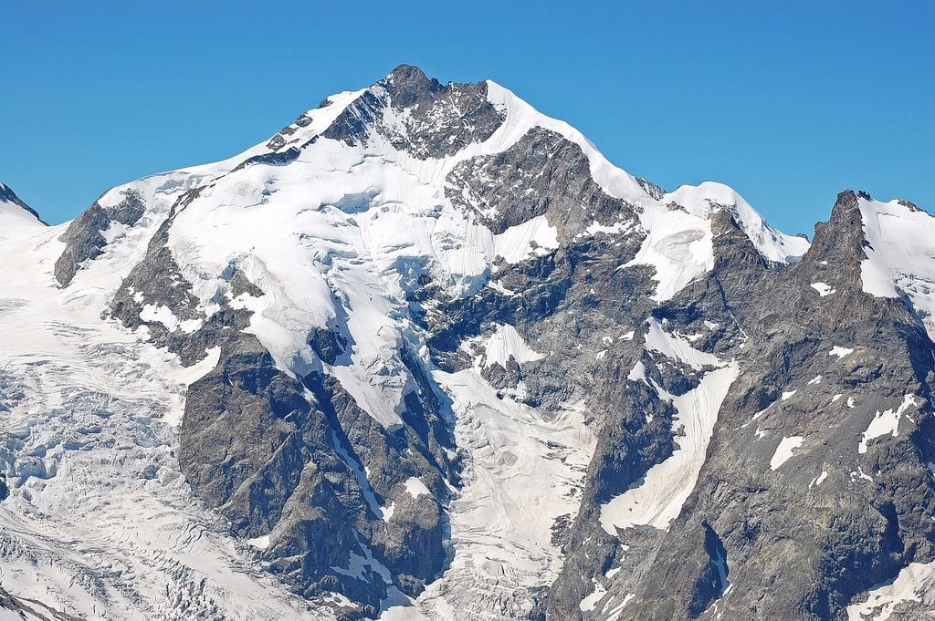 A glaciated summit with snow fields against a blue sky