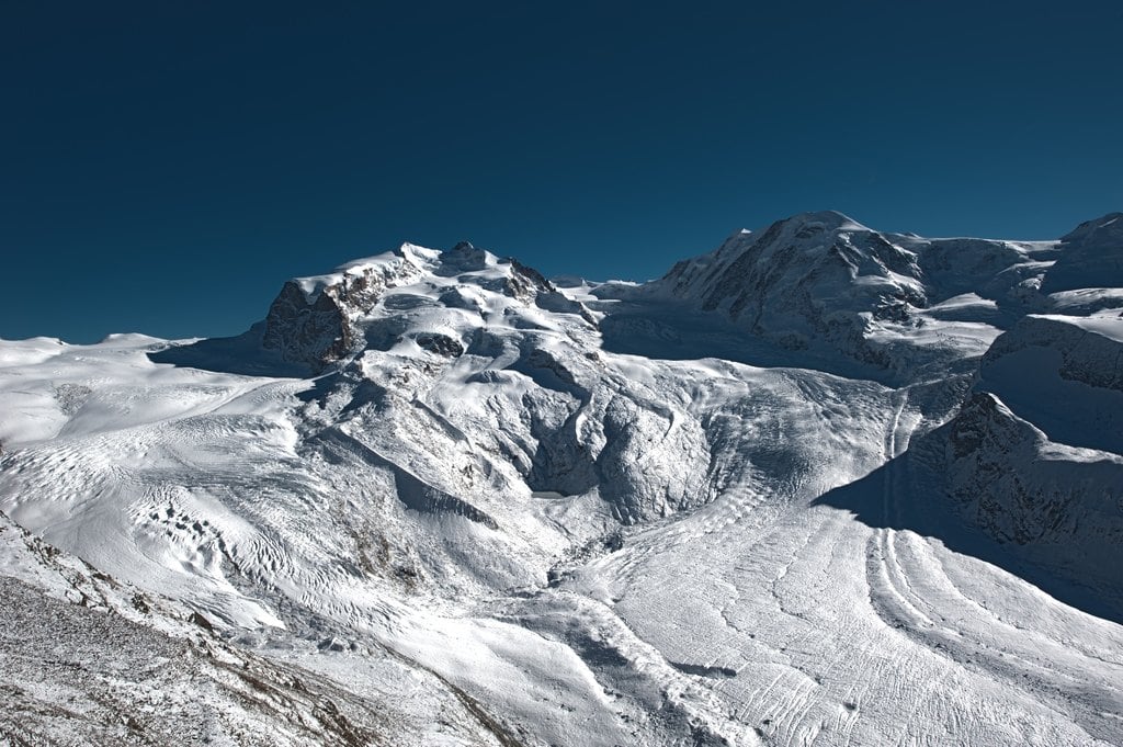 A wide glacier and snowy summits in sunlight