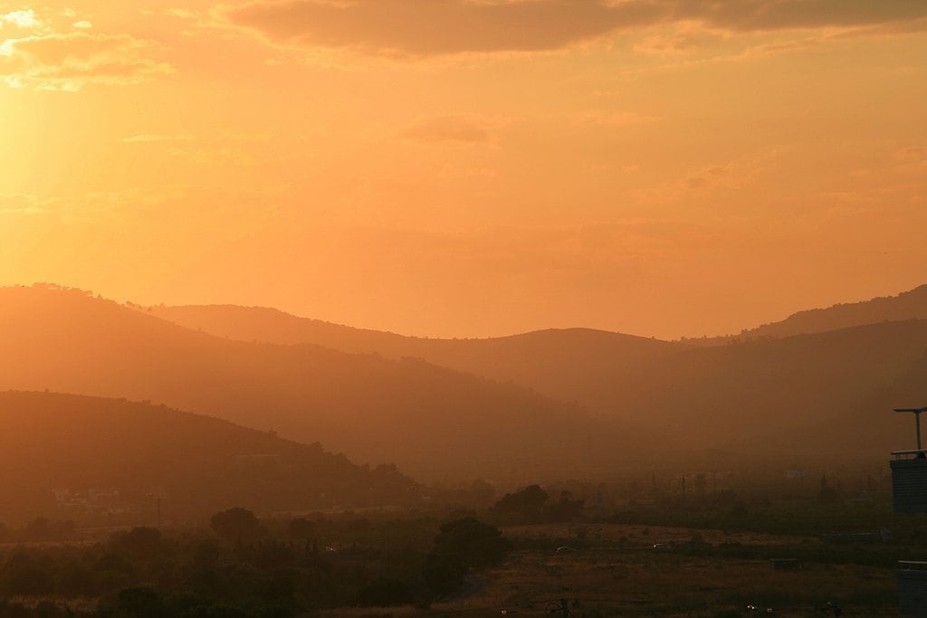 An orange sun haze over layered hills